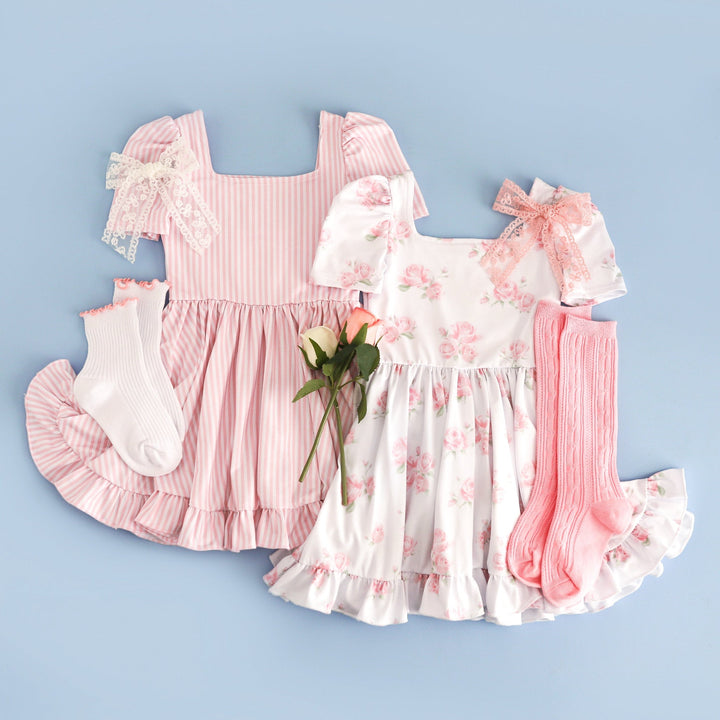 flat lay spring sister set with pastel pink pinstripe print twirl dress and white with pink floral print twirl dress paired with matching lace bows and socks