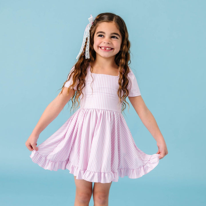 little girl in light pink and white pinstripe spring twirl dress paired with white lace haor bow with pink satin ribbon on clip