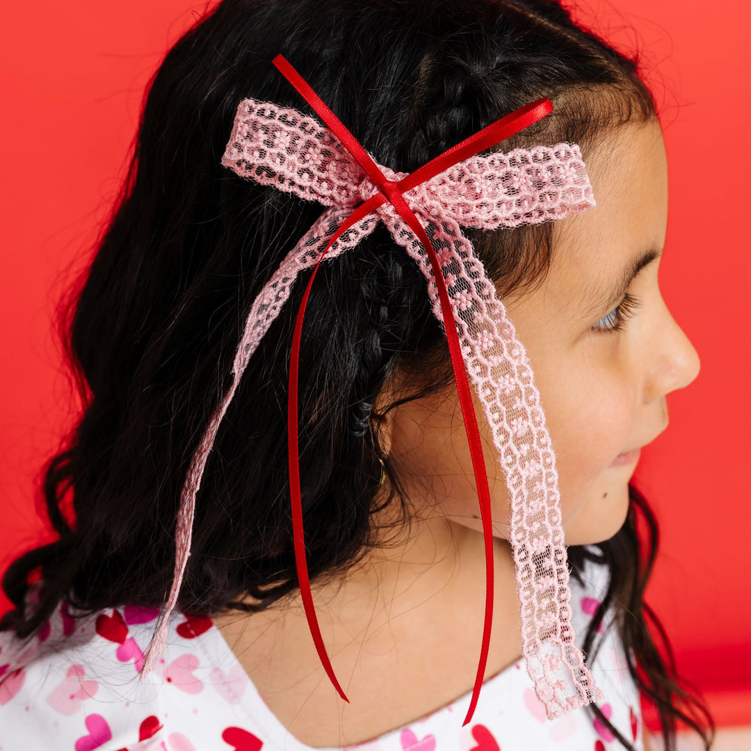 young girl with light pink lace and bright red ribbon hair bow on clip paired with heart print twirl dress