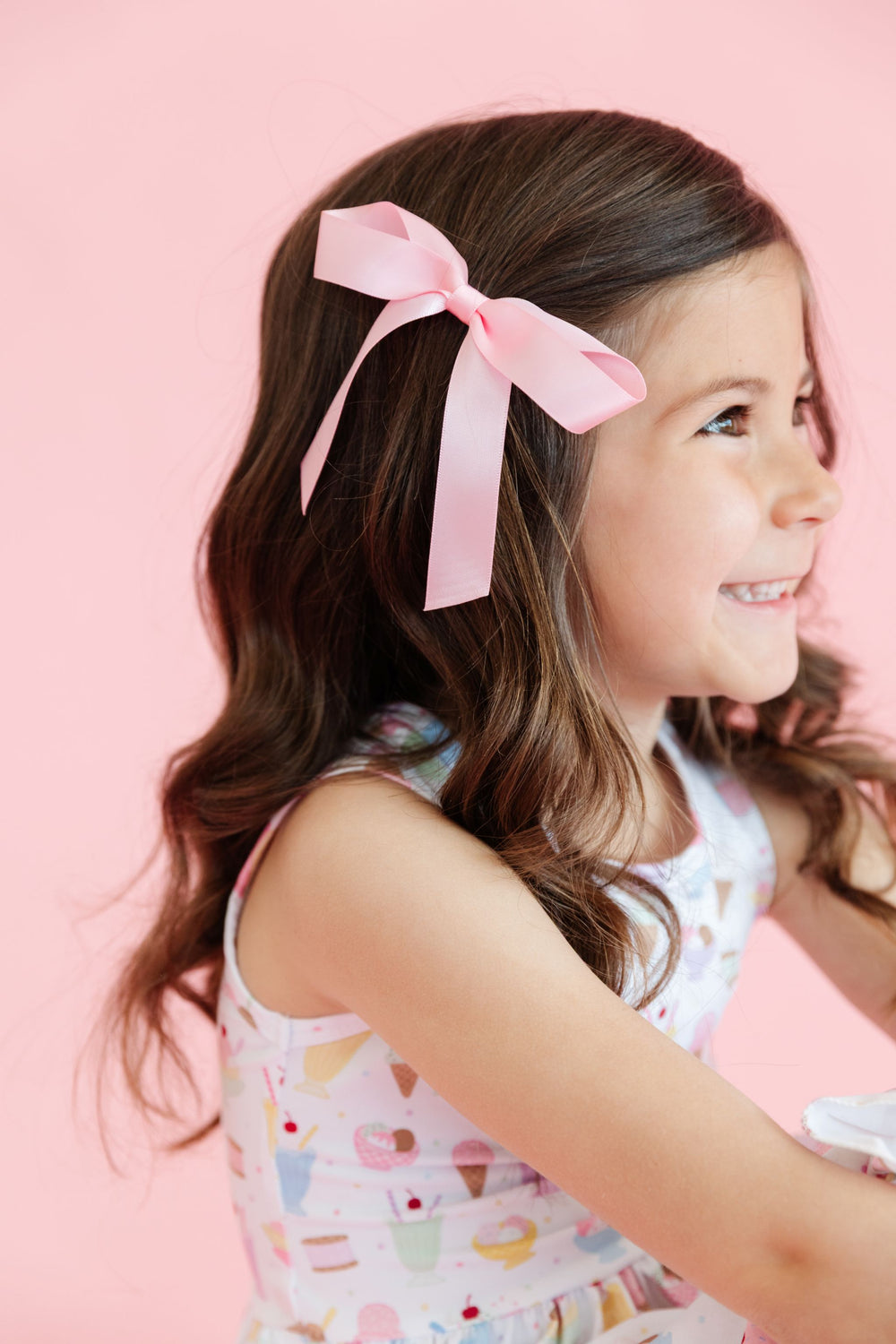 little girl with pastel pink satin ribbon bow on clip and matching sleeveless ice cream print dress for summer