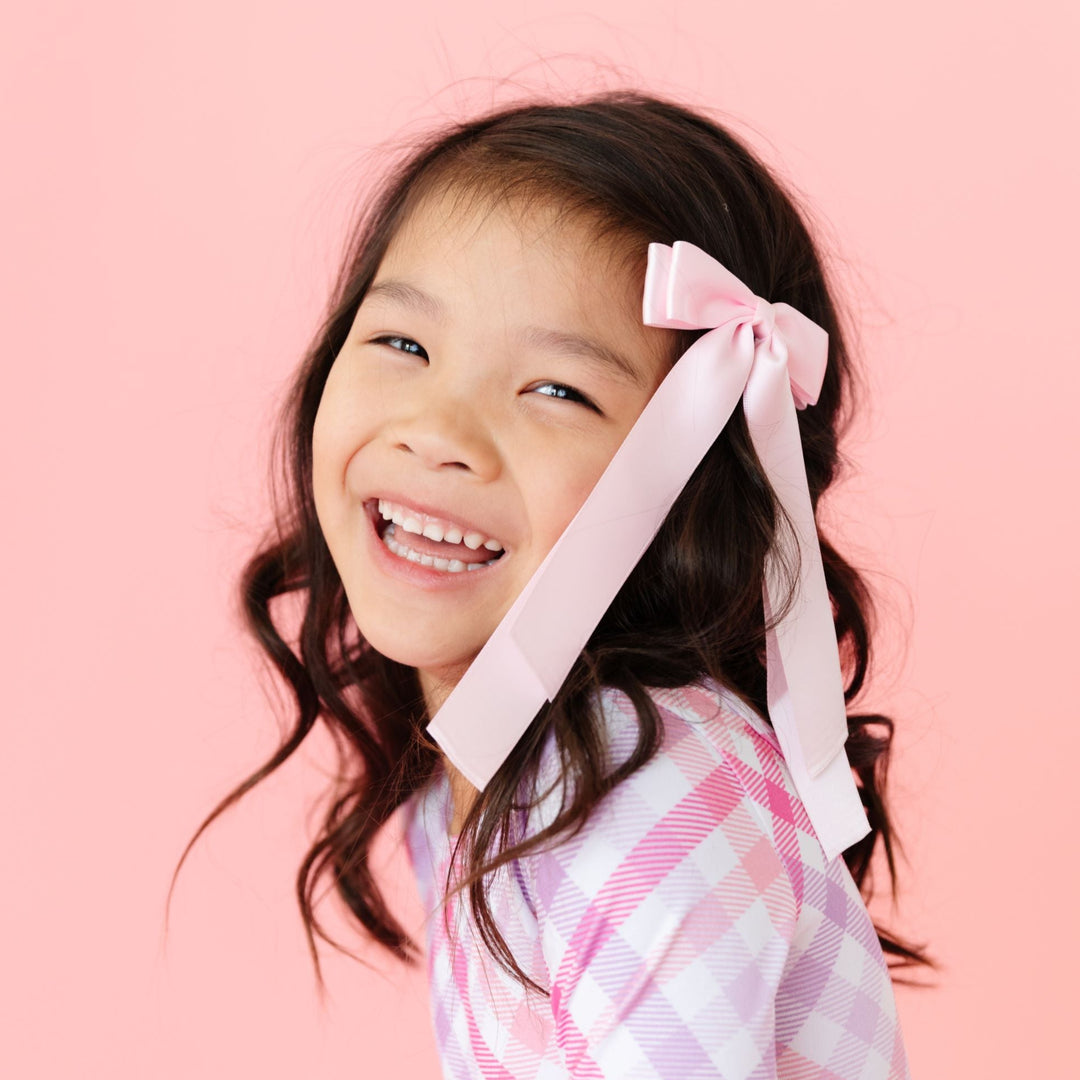 little girl in light pink satin ribbon style bow on clip and matching pink and lavender valentine's day gingham dress