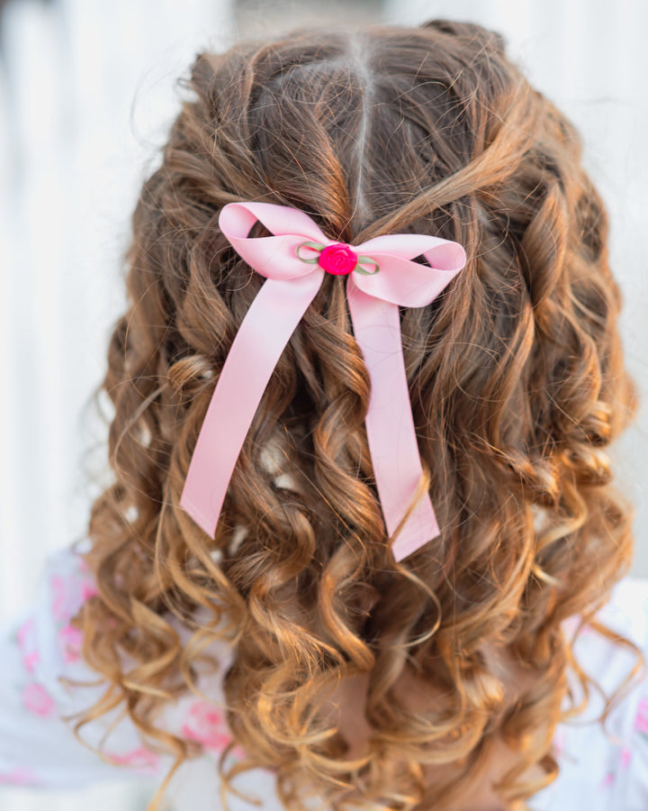 little girl with curls wearing light pink satin hair bow with bright pink rosette embellishment