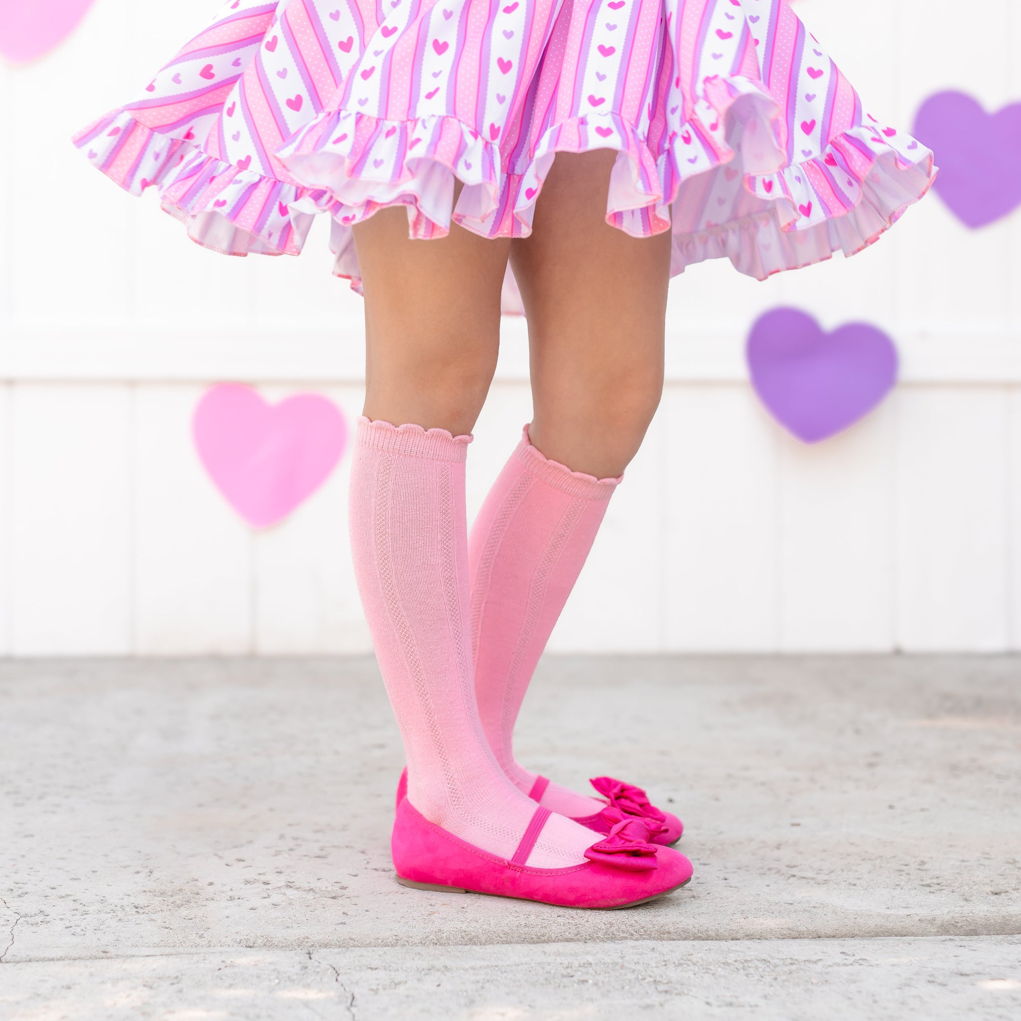 little girl in pastel pink scallop trimmed knee high socks and matching valentine's themed wallpaper twirl dress