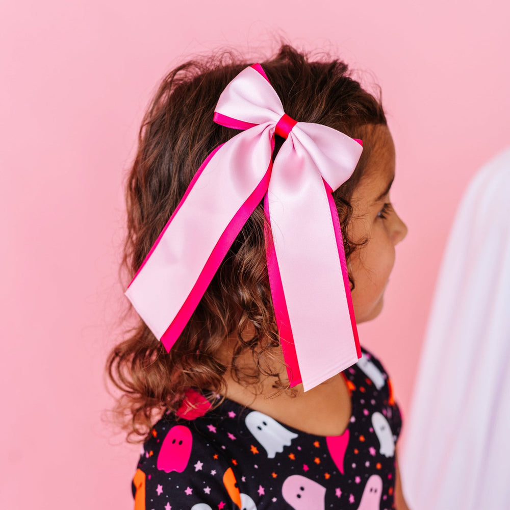 young girl in ghost print twirl dress paired with hot pink satin ribbon bow with light pink satin layered on top