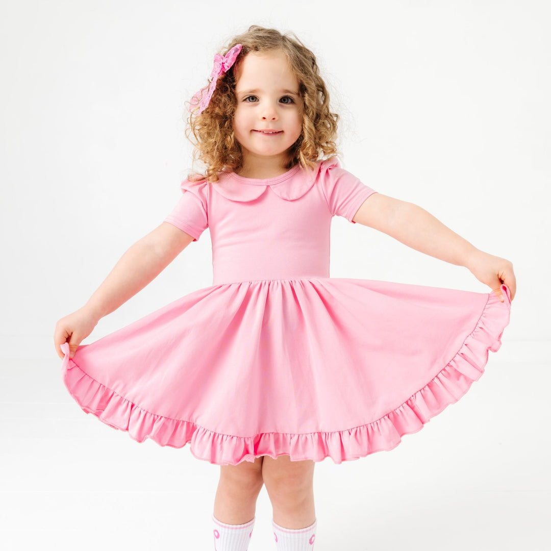 little girl in solid pastel pink short sleeve twirl dress with peter pan collar and matching pink bow and crew socks with pink bow design