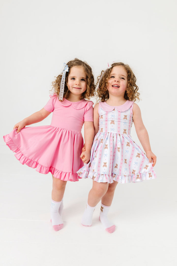 sisters in coordinating dresses with peter pan collars and matching crew socks; one in light pink short sleeve twirl and the other in vintage teddy bear print sleeveless dress