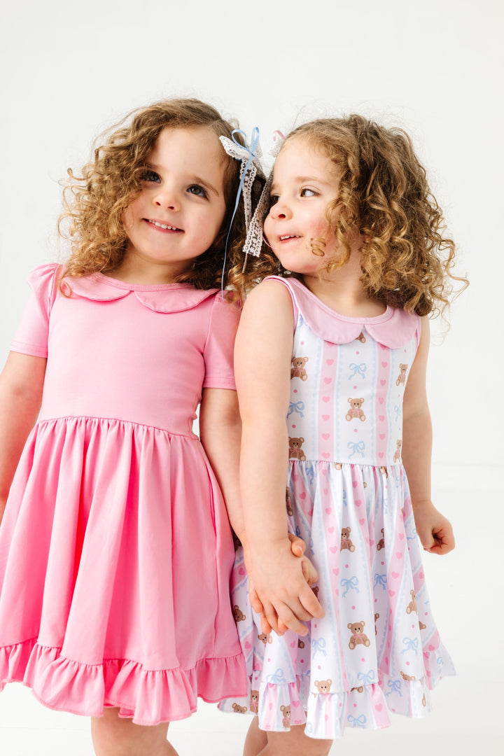 twin sisters in coordinating solid pastel pink and teddy bear print twirl dresses with peter pan collars