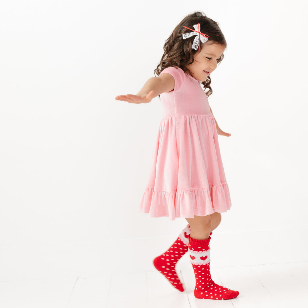 little girl in pastel pink velvet twirl dress with red Valetine's print knee highs and matching white with red ribbon lace bow 