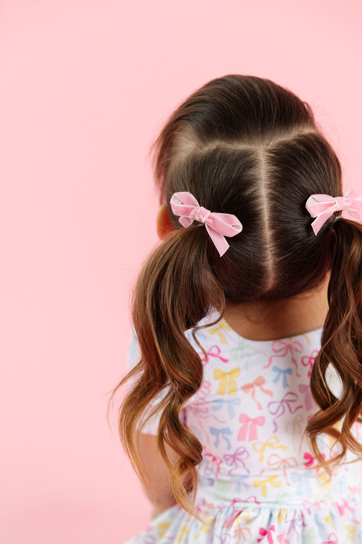 little girl with pigtails styled with light pink velvet ribbon pigtail bows on clips and matching bow print twirl dress for spring