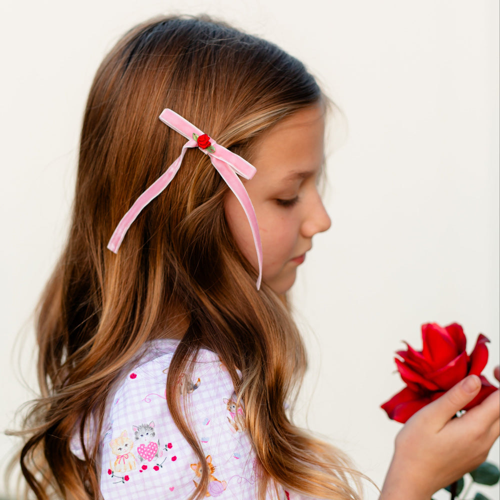 girl holding rose and wearing light pink velvet ribbon hair bow with red rosette to match Valentine's collection