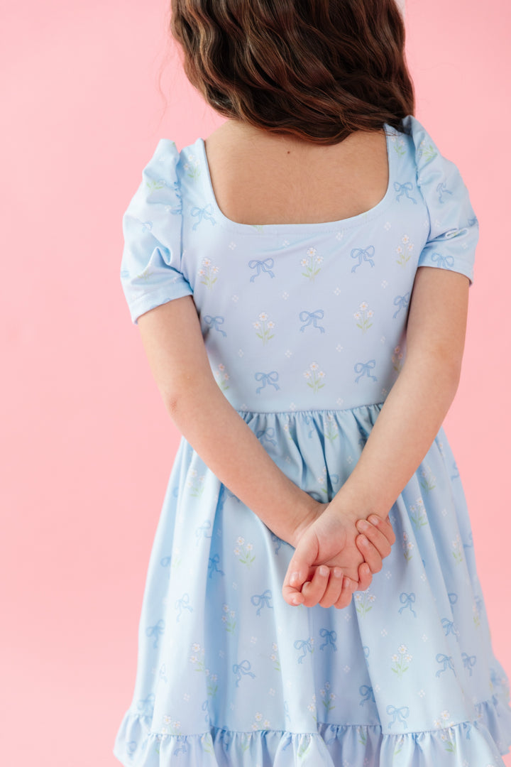 back view of square neck blue twirl dress with bows and white flower bouquets