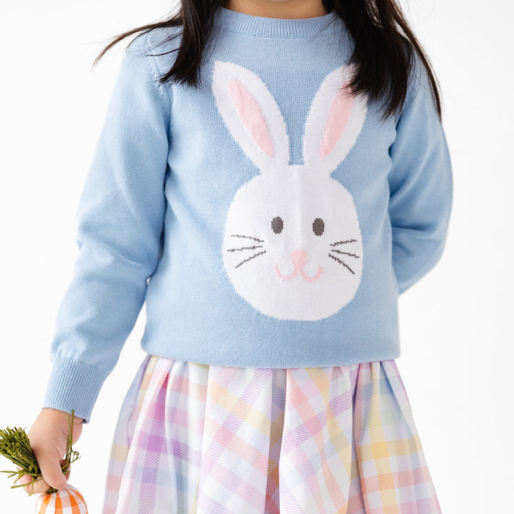 closeup of girl wearing blue pullover sweater with white bunny on it and pastel twirl dress underneath