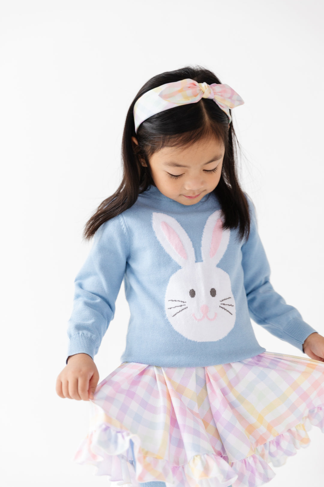 girl in easter outfit of pastel plaid dress and matching headband and blue pullover sweater with white bunny on it