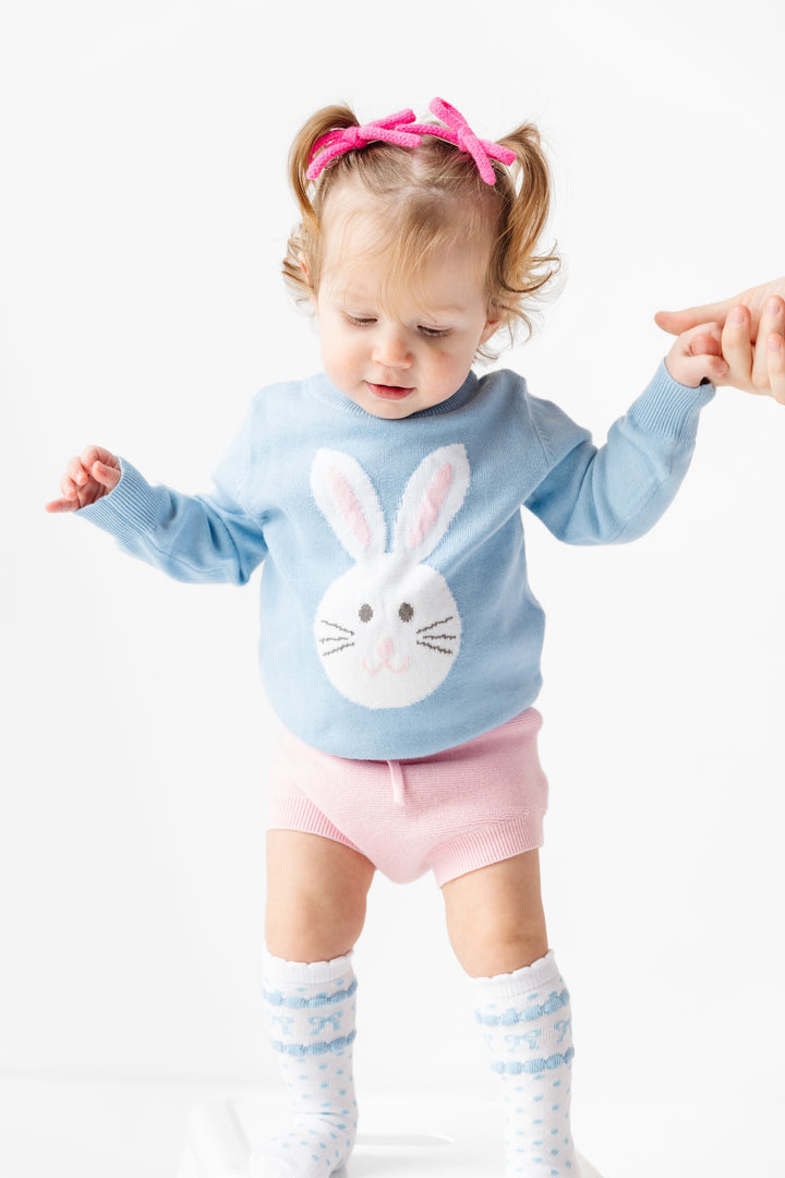 toddler girl in blue easter bunny sweater, pink bloomers and white knee high socks with blue bows on them