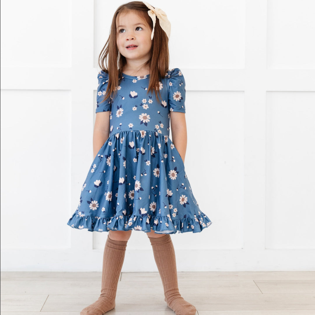 little girl in blue floral twirl dress with hands in pockets and mocha brown cable knit knee high socks