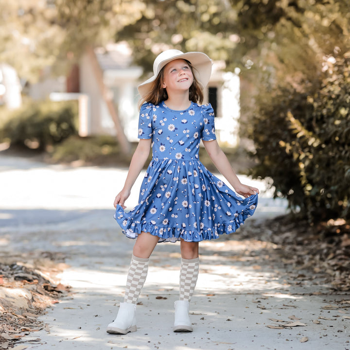 little girl outside in blue floral twirl dress and neutral checkered knee high socks and cream hat