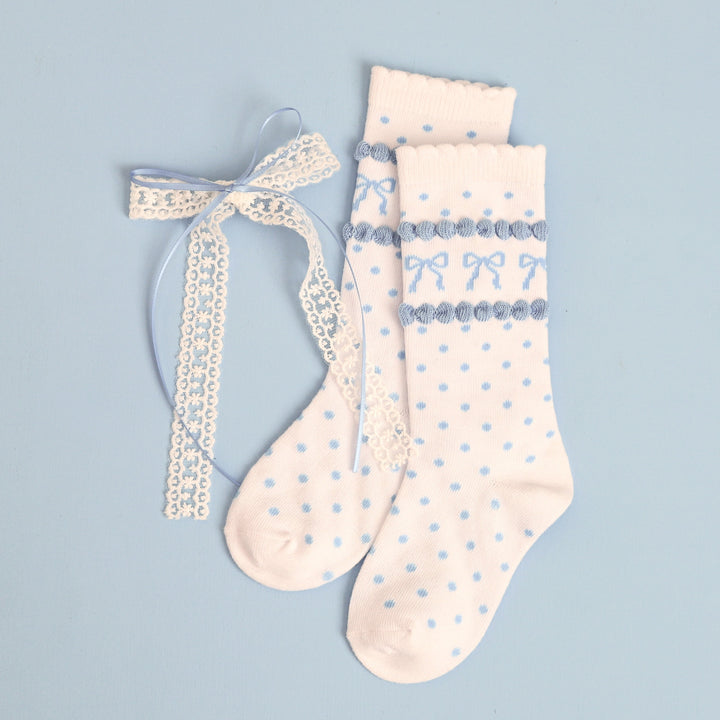 flat lay of girl's white scallop trimmed knee highs with blue bow detail and matching white lace long tail hair bow with pastel blue satin overlay