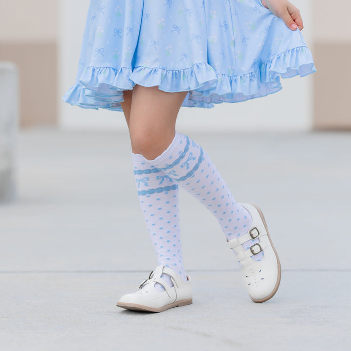 little girl in white with blue polka dot and bow print knee highs and matching blue floral spring dress