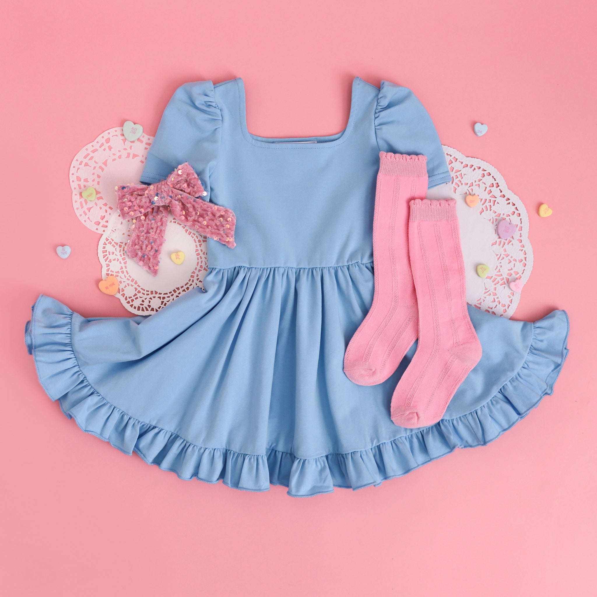 styled flat lay for Valentine's Day with blue square neck twirl dress paired with pastel pink knee highs and velvet bow with sequins.