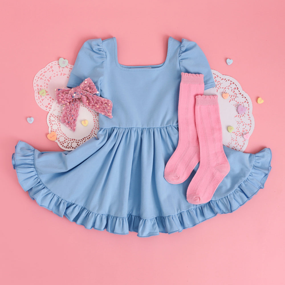 styled flat lay for Valentine's Day with blue square neck twirl dress paired with pastel pink knee highs and velvet bow with sequins.