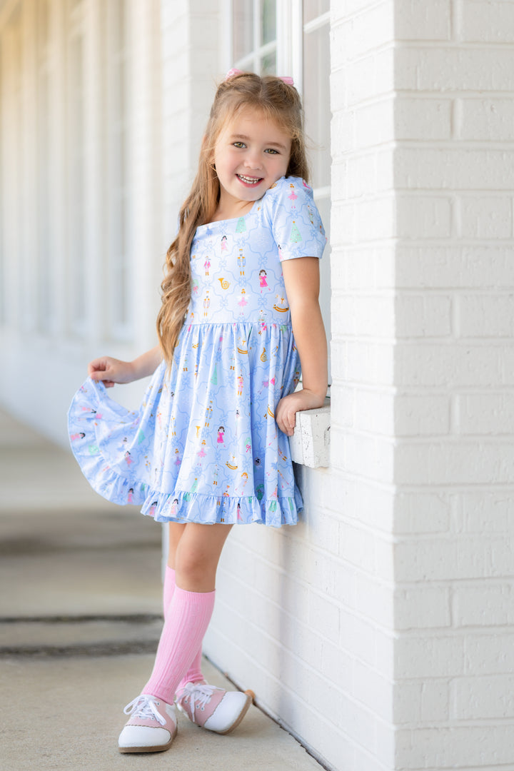 little girl posing in light blue nutcracker print twirl dress with matching light pink cable knit knee highs and saddle shoes