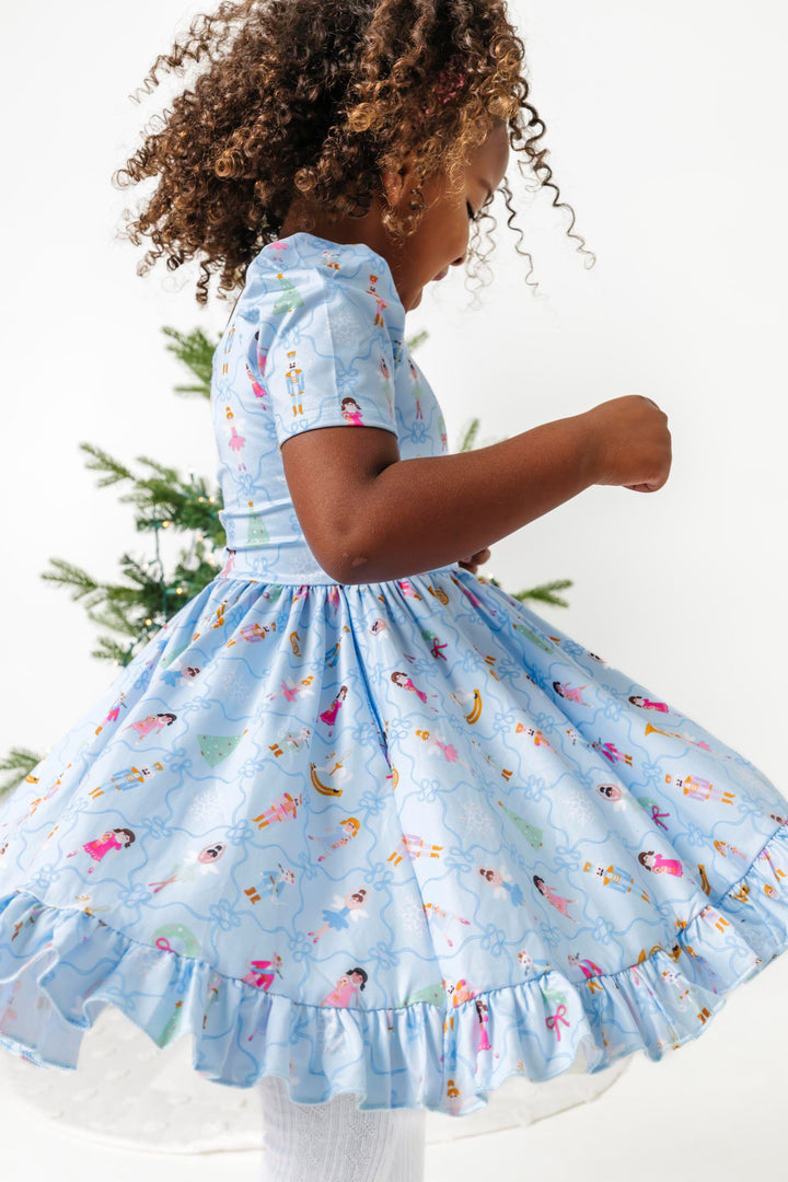 little girl twirling in light blue twirl dress with nutcracker themed print and dainty blue ribbon design