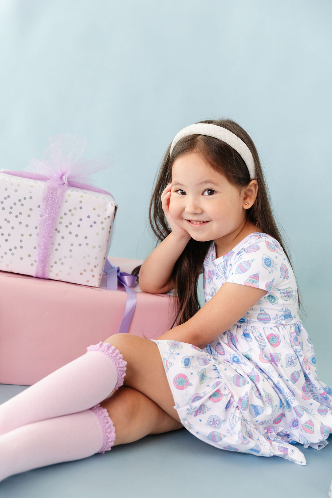 little girl in Christmas ornament print dress with a variety of pastel colors, light purple knee highs and sparkly silver headband