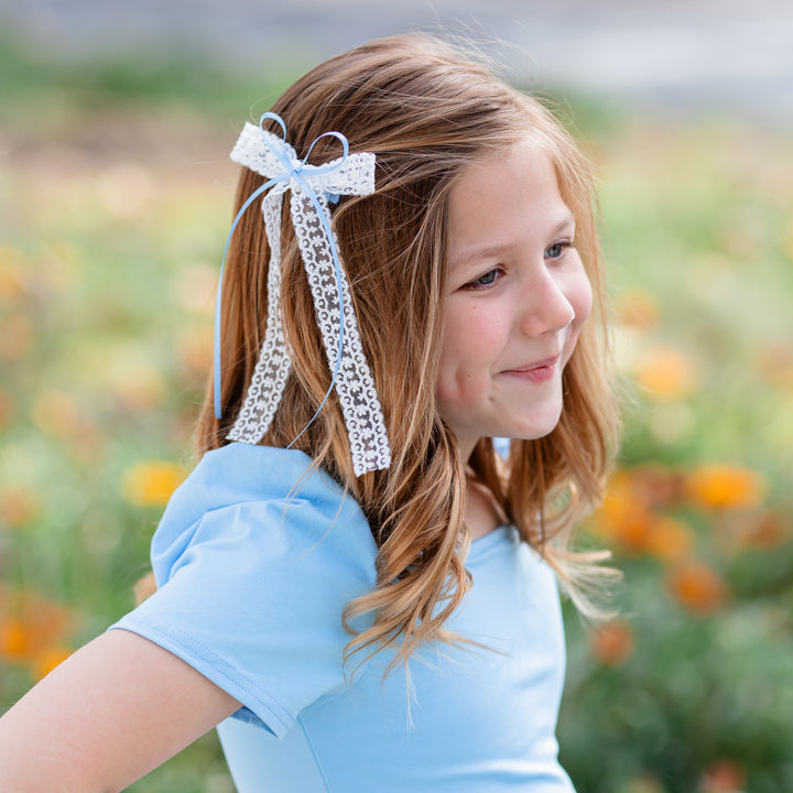 little girl in spring garden with white and blue lace and satin ribbon hairbow and matching blue cotton twirl dress