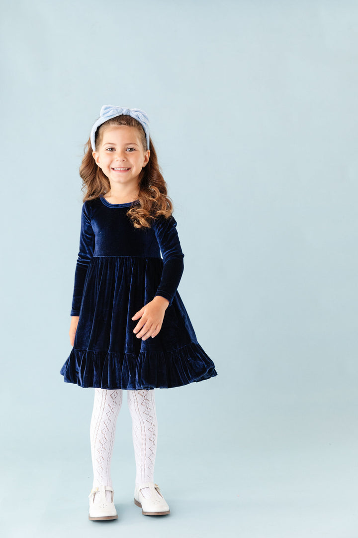 little girl wearing navy velvet party dress with white pointelle knit tights and velvet headband