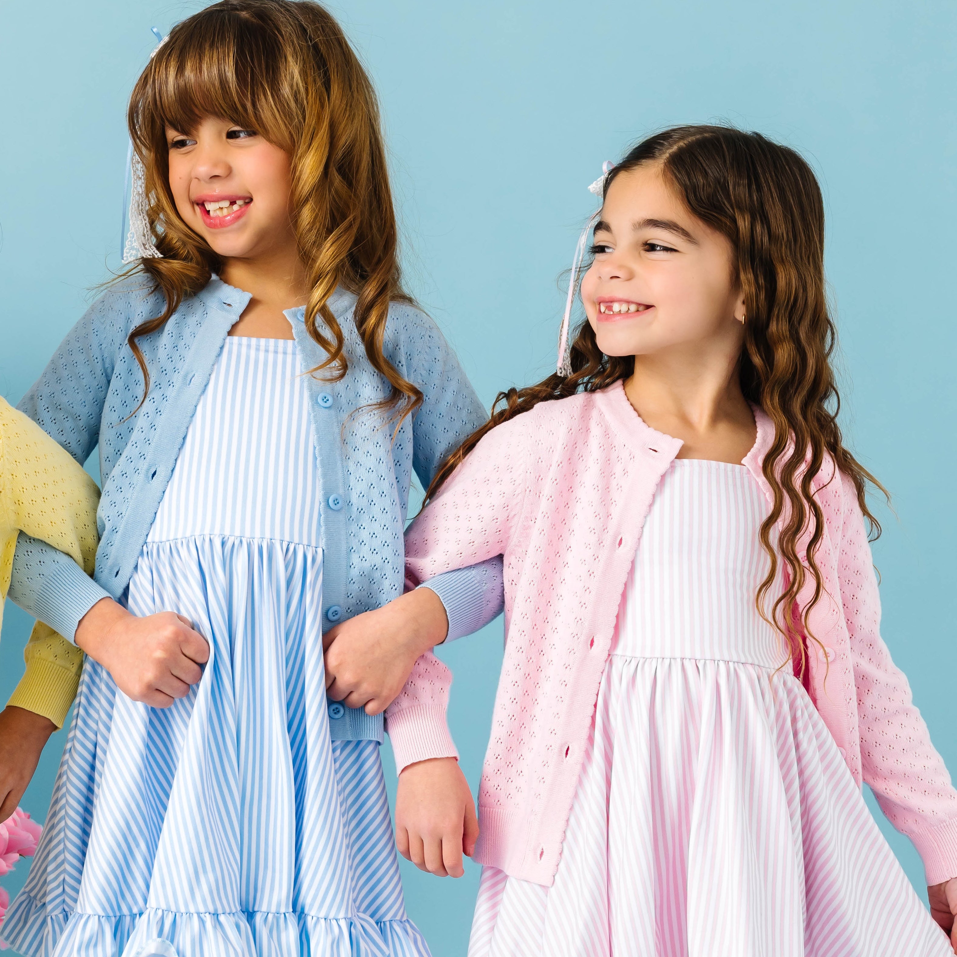 Two young girls wearing matching cardigans and dresses against a blue background