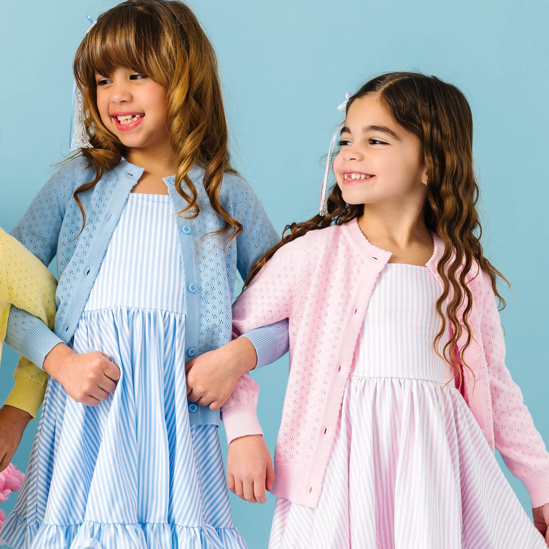 Two young girls wearing matching cardigans and dresses against a blue background