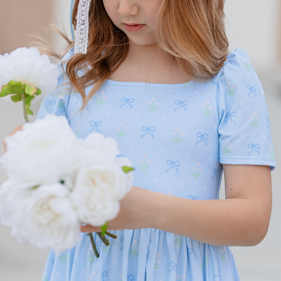 close up of girl wearing square neck dress with blue background and blue bows and white flower bouquets