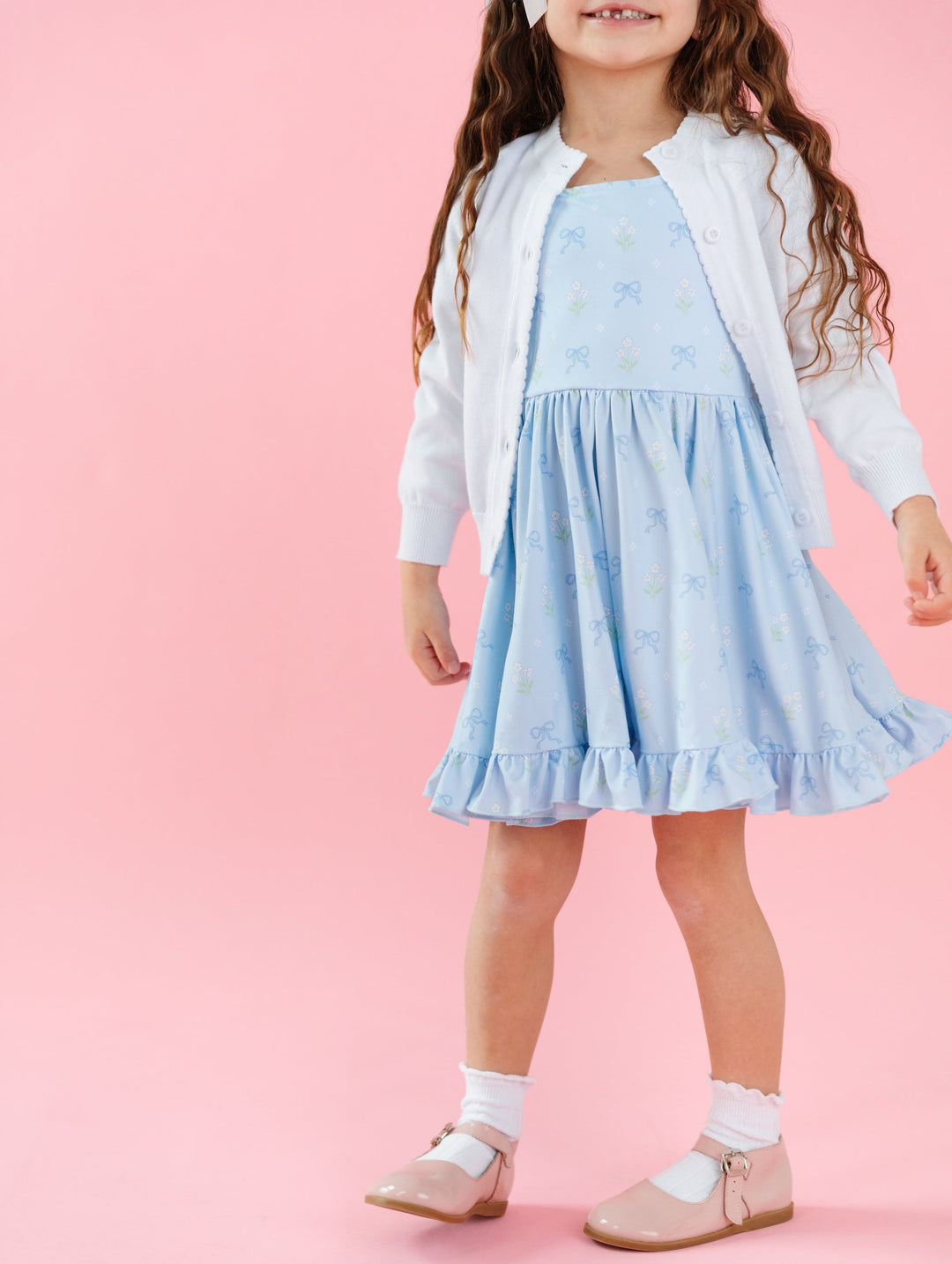 little girl in blue twirl dress with bows and white flowers printed on it and matching white scallop cotton sweater