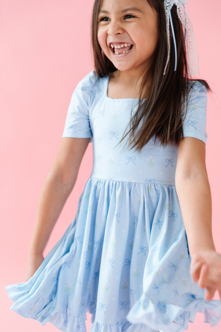 girl smiling in blue square neck dress with petite white flowers and blue bows