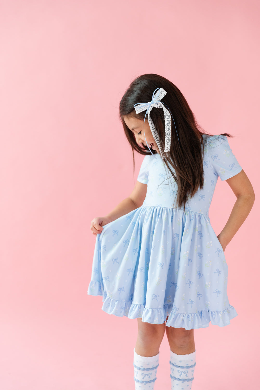 girl in blue square neck dress with petite white flowers and blue bows and matching white knee high socks with bows and white lace bow in hair