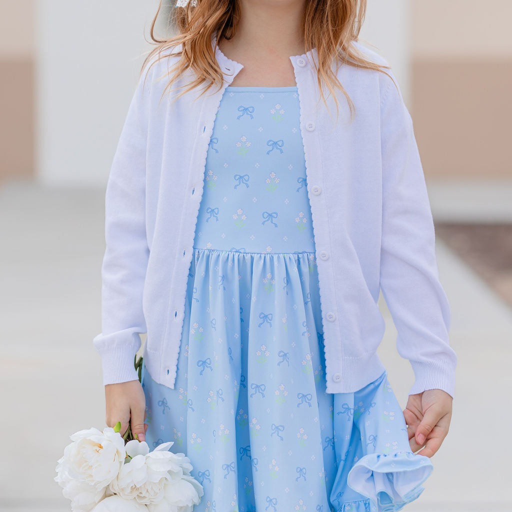 closeup of girl in spring blue twirl dress with flower and bow print paired with white button front knit cardigan 