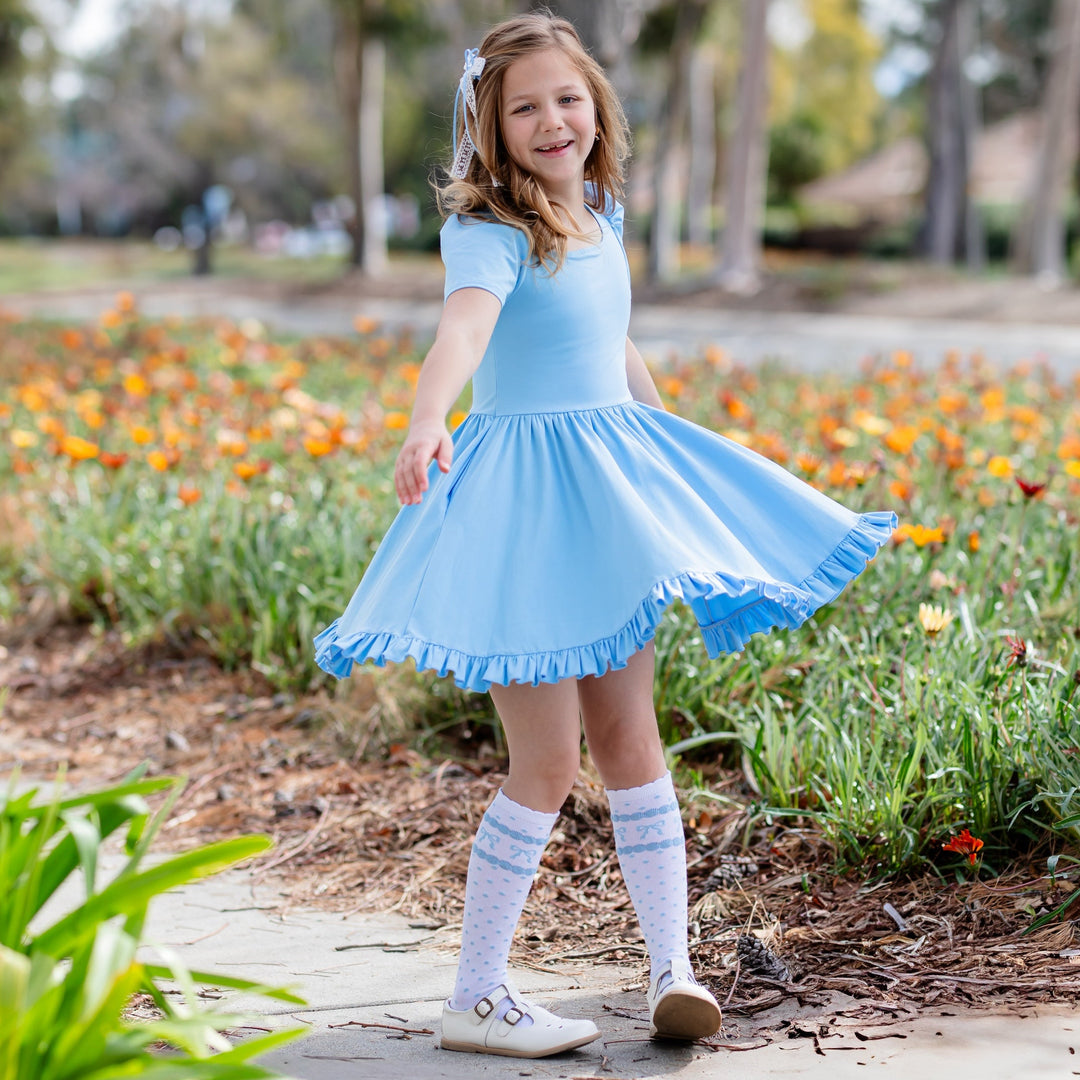 girl spinning in blue twirl dress with square neck and puff sleeves and matching knee high socks with blue bows printed