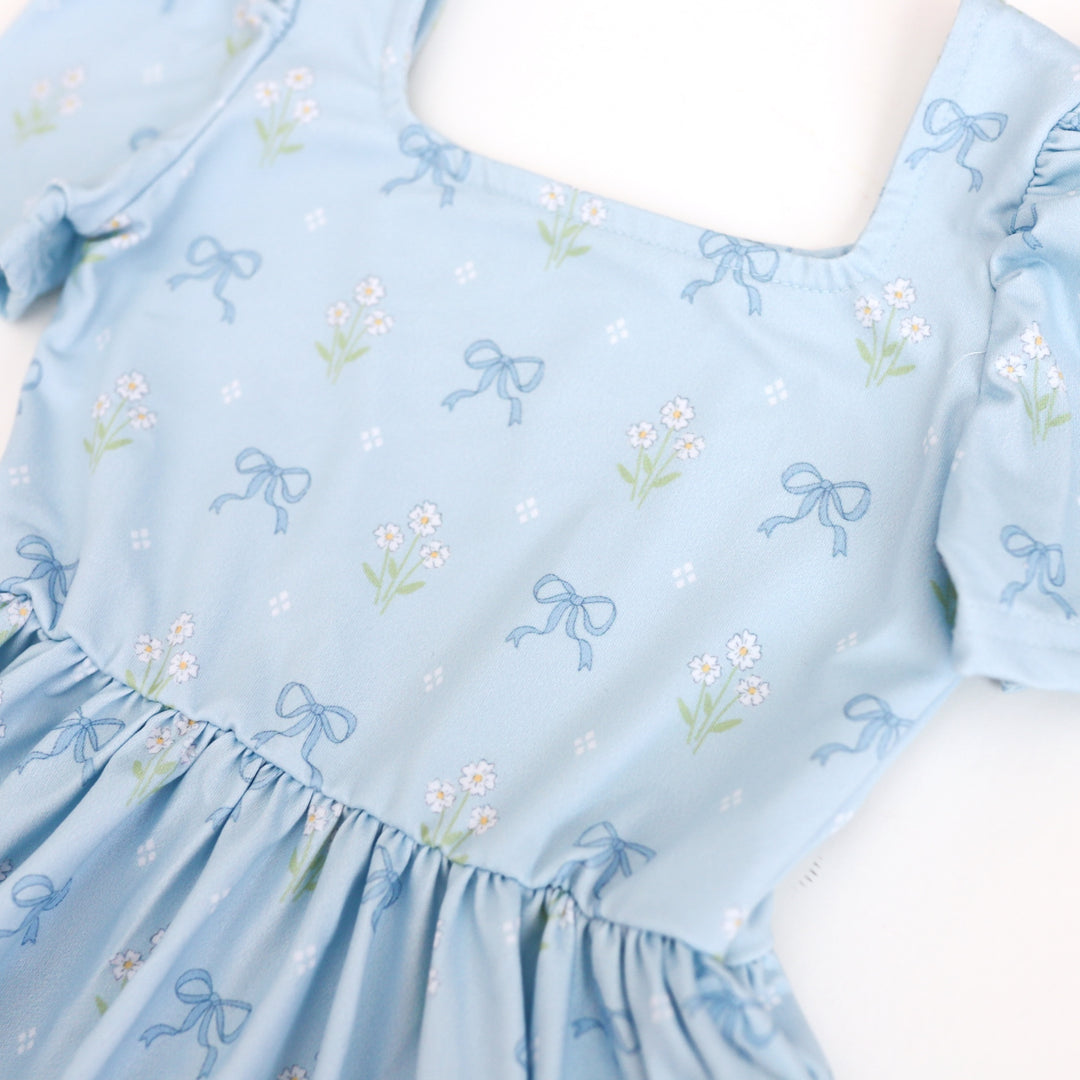 detail photo of girl's blue square neck dress with petite white flowers and blue bows