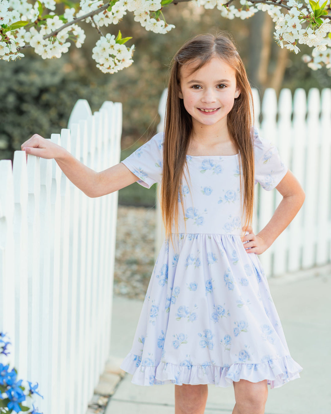 young girl by garden gate wearing white square neck twirl dress with dreamy blue floral print for spring