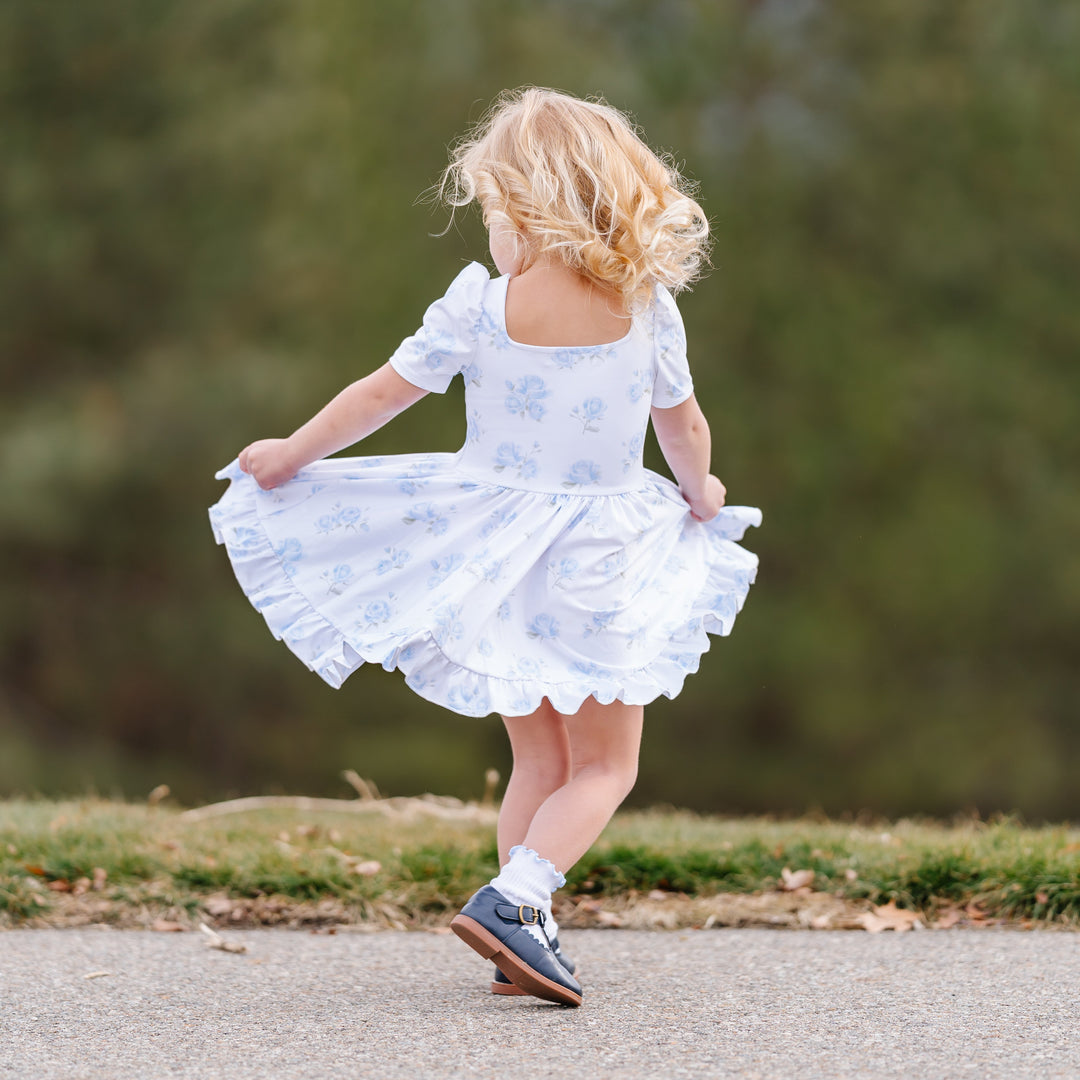little girl twirling outside in white spring twirl dress with light blue rose resign and matching blue trimmed midi socks