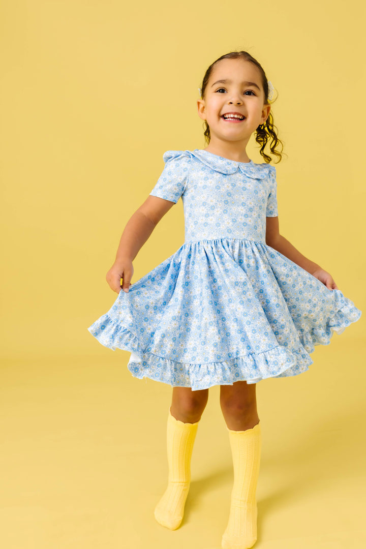 little girl twirling in blue spring floral dress with peter pan collar and matching pastel yellow knee socks with scalloped trim