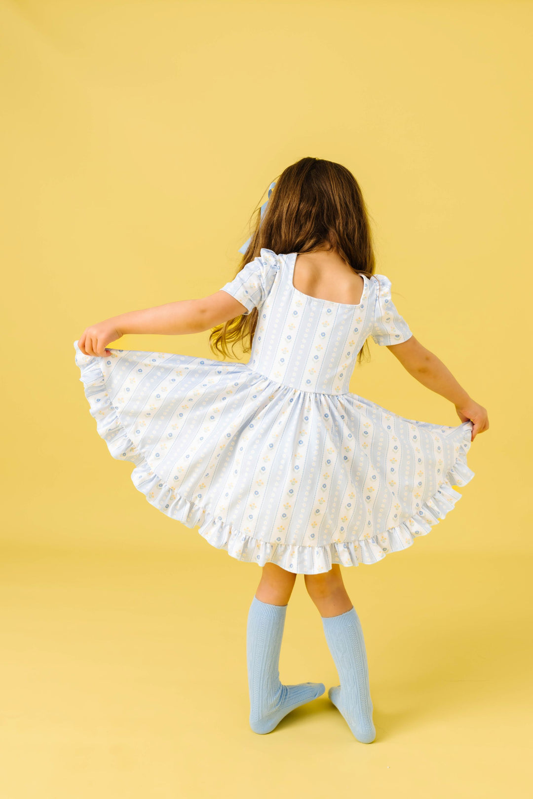 back view of little girl twirling in light blue wallaper floral inspired spring print twirl dress with matching knee highs