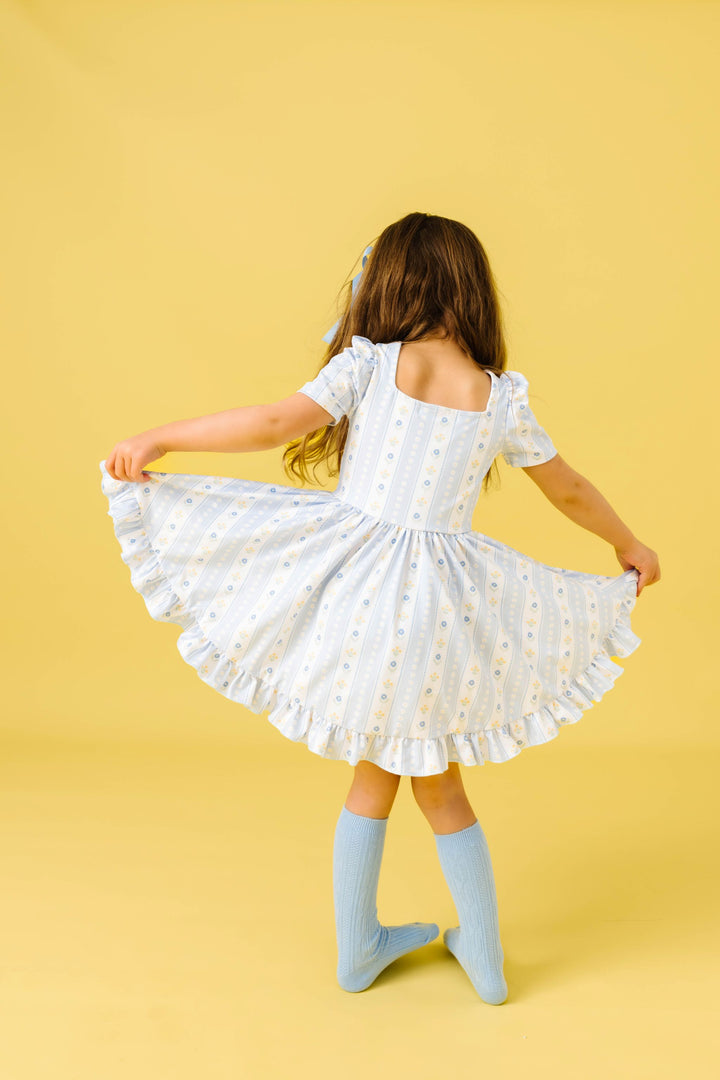 back view of little girl twirling in light blue wallaper floral inspired spring print twirl dress with matching knee highs