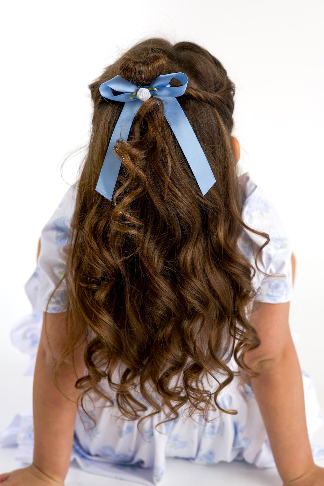 young girl with hair pulled back in pastel blue satin bow with white rosette on clip to match blue floral twirl dress