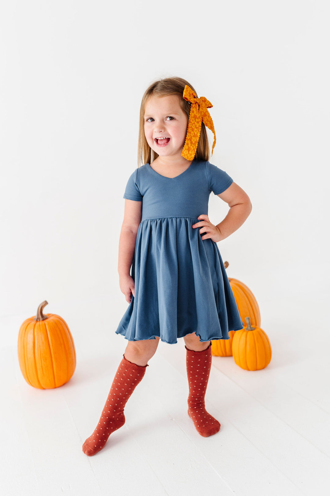 little girl wearing dusty blue dress with rust knee high socks and yellow hair bow