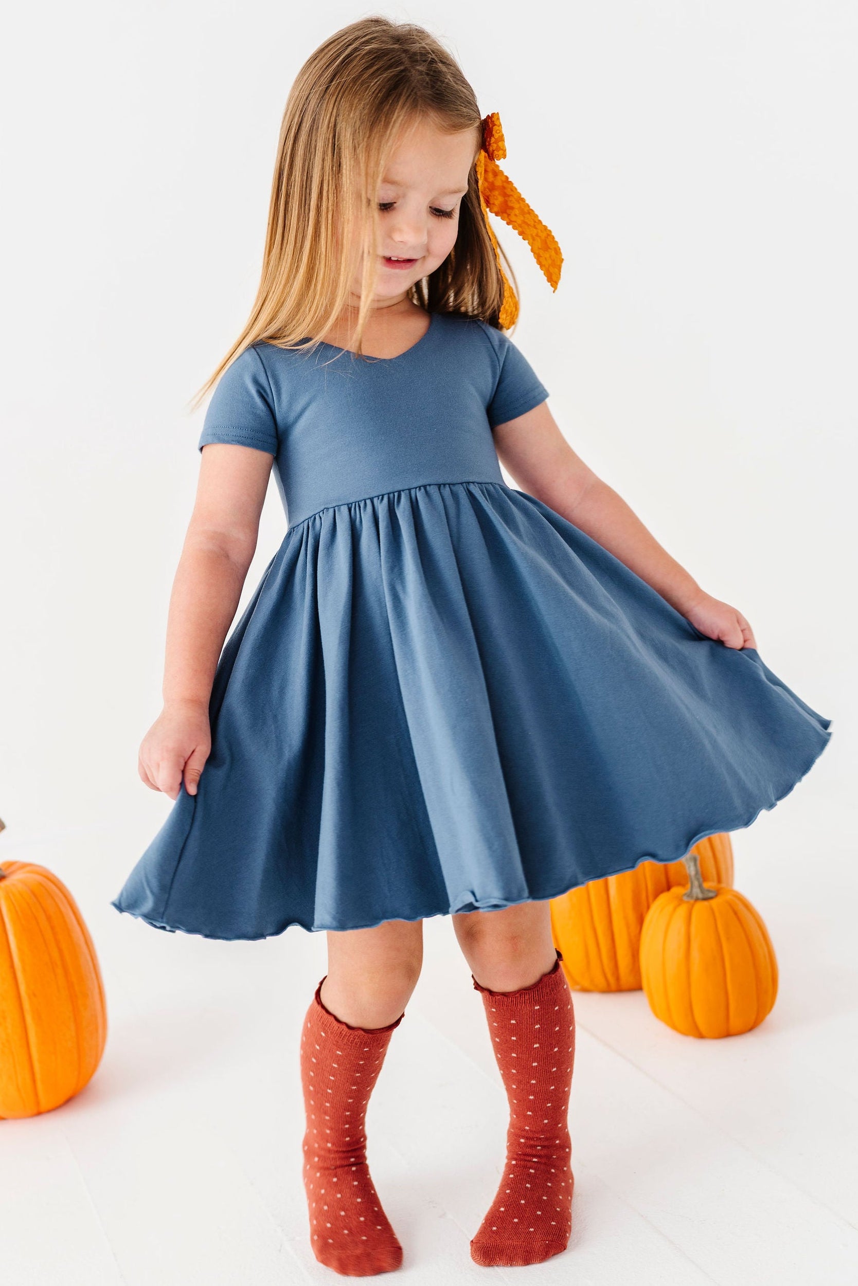 little girl twirling in blue v neck dress with rust polka dot knee high socks