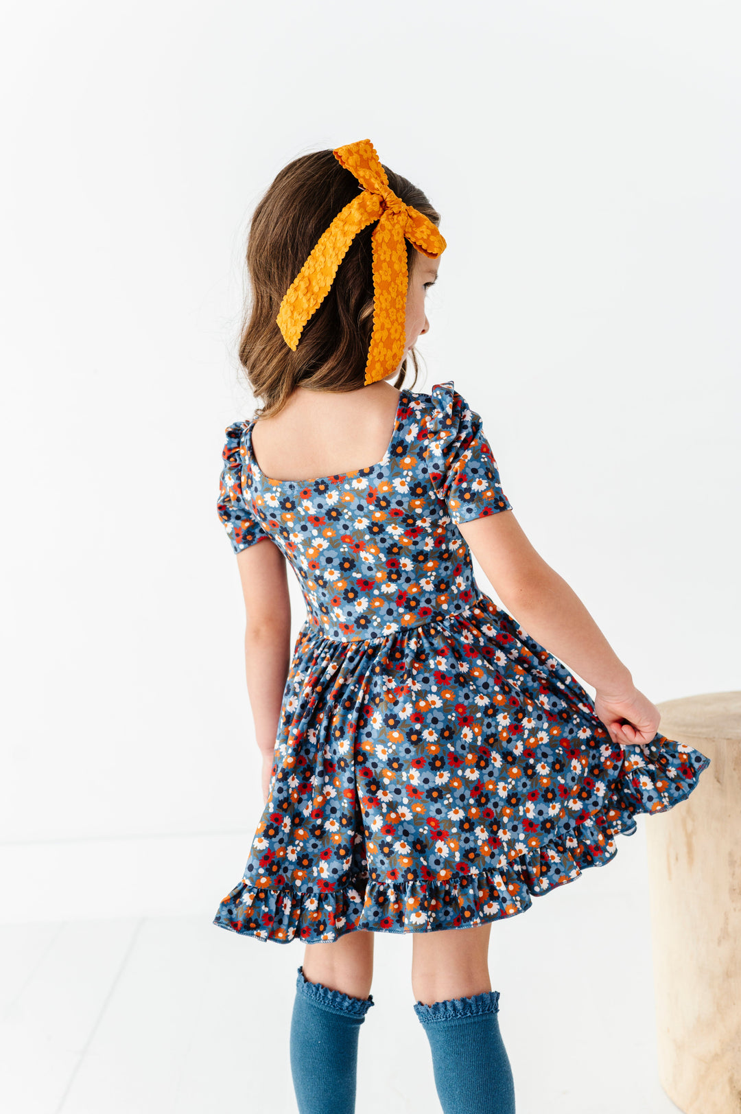 young girl in square neck blue fall floral twirl dress paired with matching blue lace top knee socks and mustard jacquard hair bow