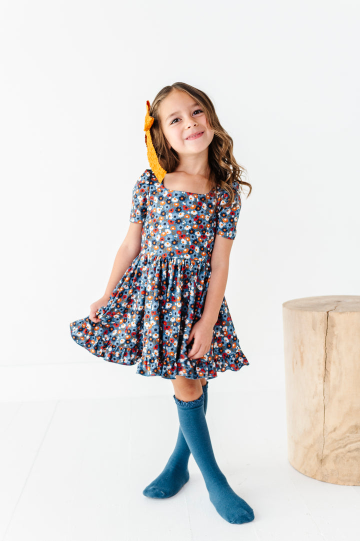 young girl in blue fall floral twirl dress paired with mustard hair bow and matching blue lace top knee socks