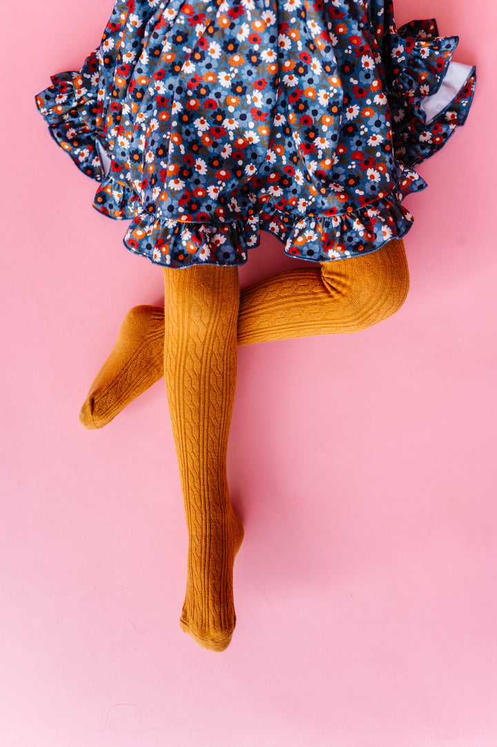 little girl sitting in blue fall floral print dress and matching mustard cable knit tights