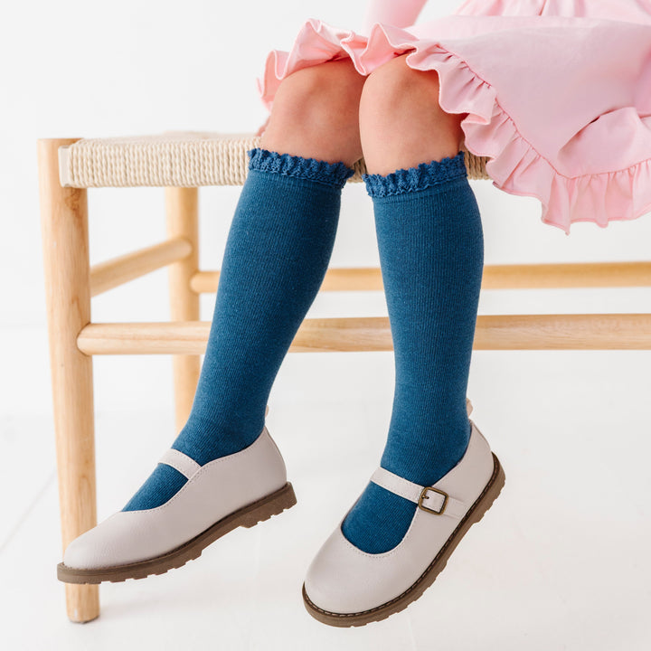 young girl sitting on bench in blue knee socks with lace trim paired with ivory mary janes and light pink twirl dress
